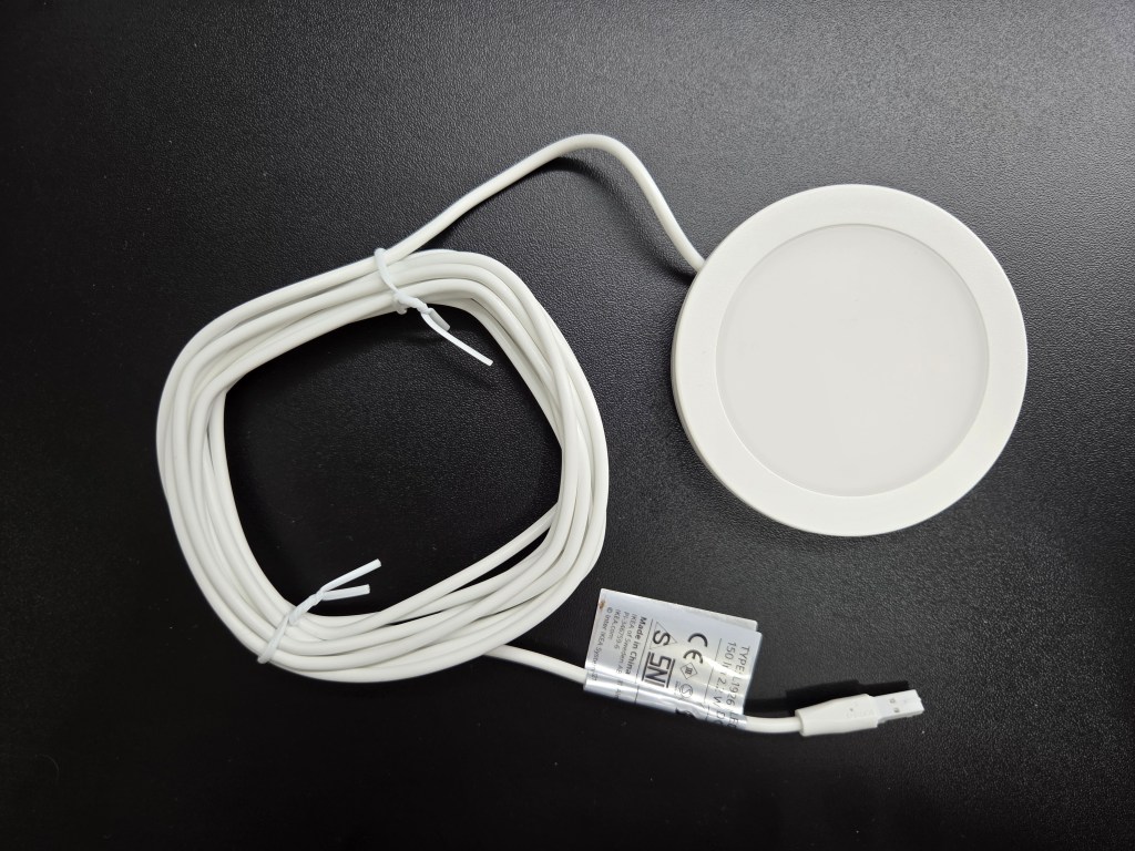 Biały okrągły podładunek z kablem USB, leżący na czarnym tle.